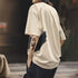 Person wearing a beige oversized t-shirt with a tattoo on the arm, standing outdoors.
